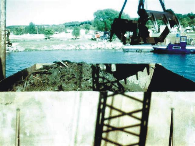 Wood debris is deposited onto barge and offloaded at shore.